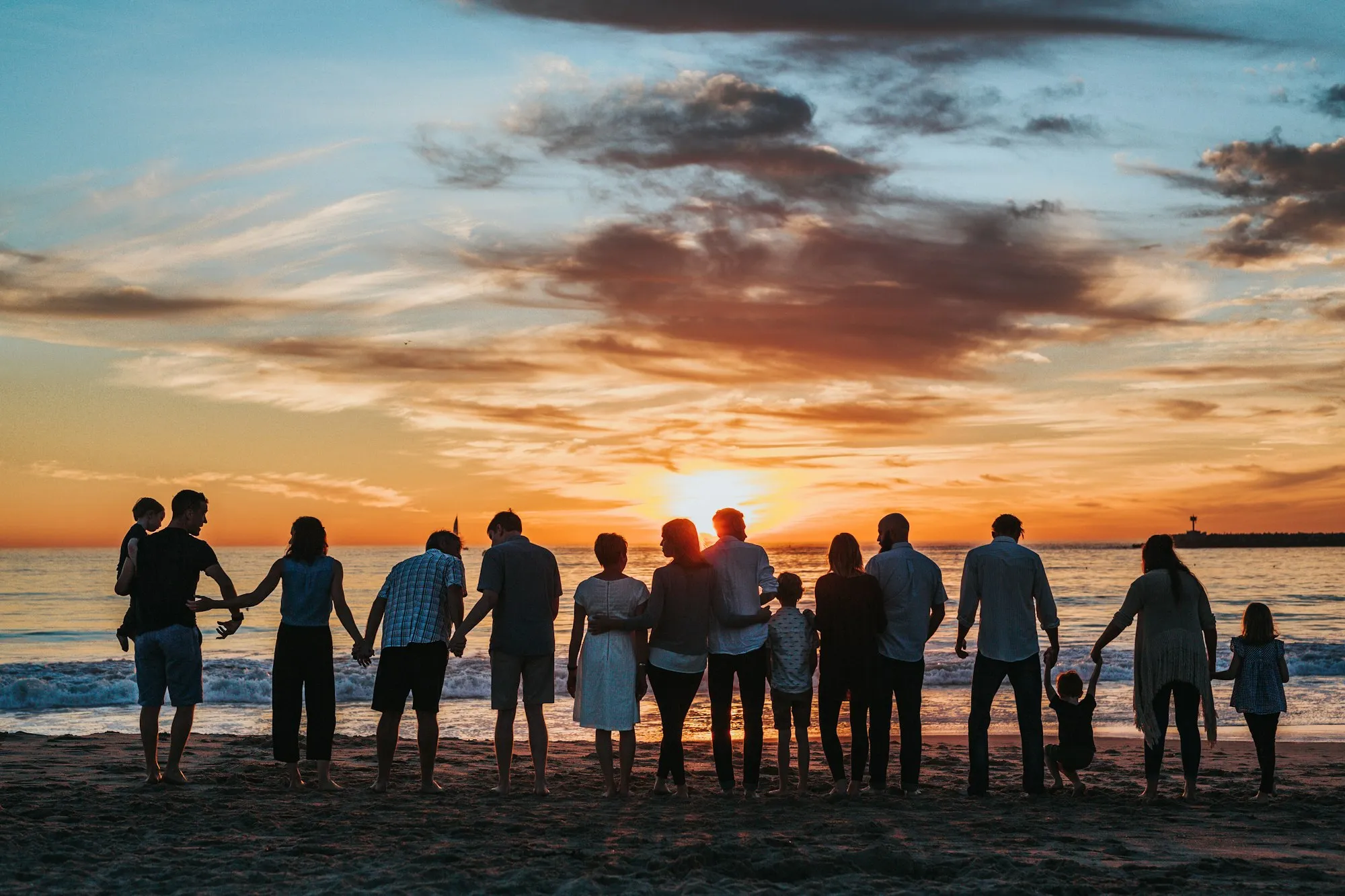 Three generations of a family standing hand in hand on the shore at sunset, watching the last light over the sea.